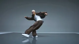A male street dance expert, white buzz cut, wearing small gold hoop earrings and a gold rope chain. Dressed in a dark br