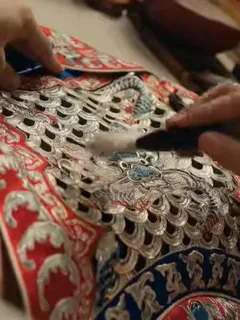 An elder Peking Opera craftsman guides an apprentice in making traditional headwear and costumes, symbolizing the passing of heritage.