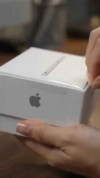 Elegant hands unboxing a silver Apple device, revealing its compact size, and demonstrating its portability by fitting it into a jeans pocket.