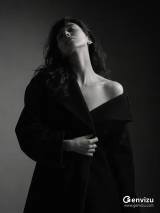 Black-and-white editorial portrait of a young East Asian woman with dramatic lighting, wearing a heavy black coat against a dark wall.