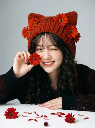 Professional studio portrait of a young Vietnamese model in a luxury magazine editorial, wearing a vibrant reddish-orange cat ear beanie with daisies.