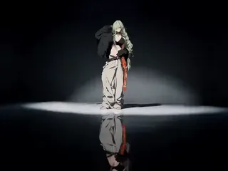 High-fashion editorial film still, featuring a model in a confident pose against a minimalist studio backdrop with dramatic lighting and a reflective floor.