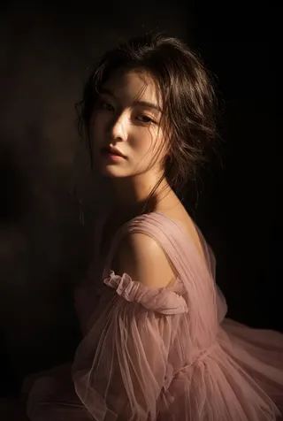 A moody portrait of a young East Asian woman with a contemplative gaze, wearing a dusty pink off-the-shoulder tulle gown in dramatic directional lighting.