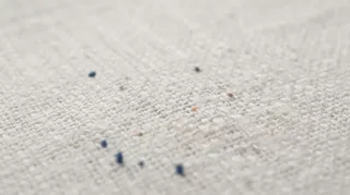 Extreme macro shot of colorful threads self-weaving into satin stitches on a woven cotton shirt fabric to form a logo.