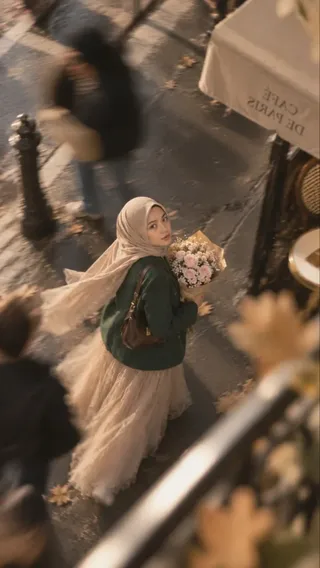 A young Southeast Asian woman wearing a taupe-beige hijab and an emerald green blazer, walking near the Eiffel Tower in Paris, with motion blur on the background.