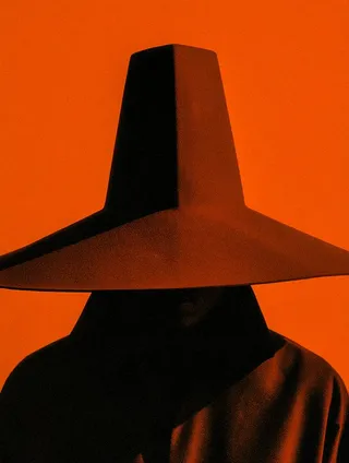 A minimalist photographic portrait of a silhouetted figure wearing a wide-brimmed hat against a vibrant orange textured background.