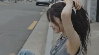 Grainy, handheld footage of a young Korean woman in a faded crop top and jeans, smiling and interacting with her environment in a residential alleyway and yard.