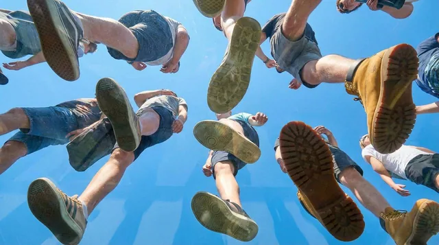 View from under a plane of completely transparent plexiglass. We are looking straight up. Many people are walking on the