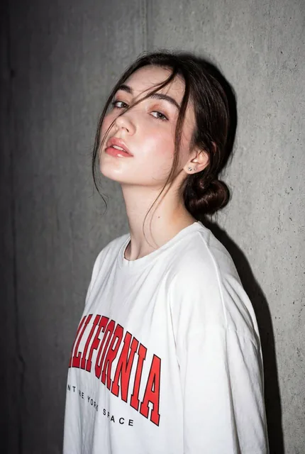 A high-resolution, close-up editorial-style portrait of a young woman standing against a textured gray concrete wall, ca