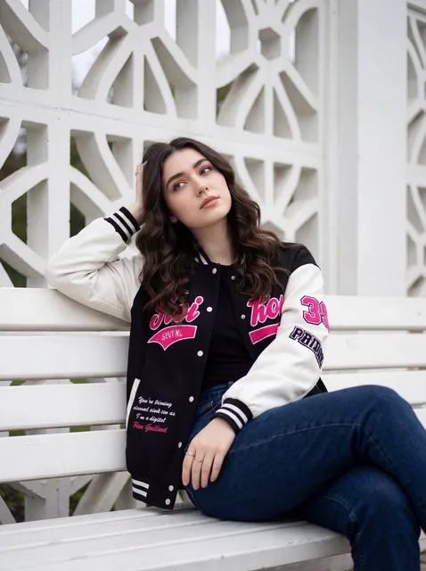 A young woman is sitting casually on a white wooden bench, positioned slightly off-center, with her legs crossed and her