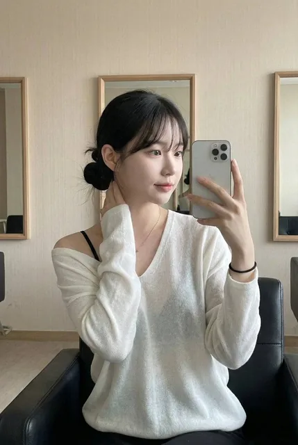 This photo captures a highly atmospheric indoor Mirror Selfie. It freezes a moment of a young Asian woman in a relaxed s