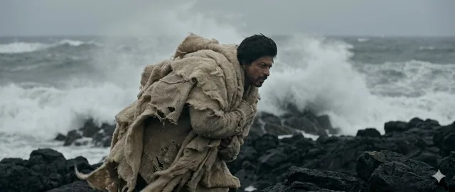 Wide shot, subject acts as an anchor against a raging wind. Standing on a jagged black rock coastline, waves crashing be