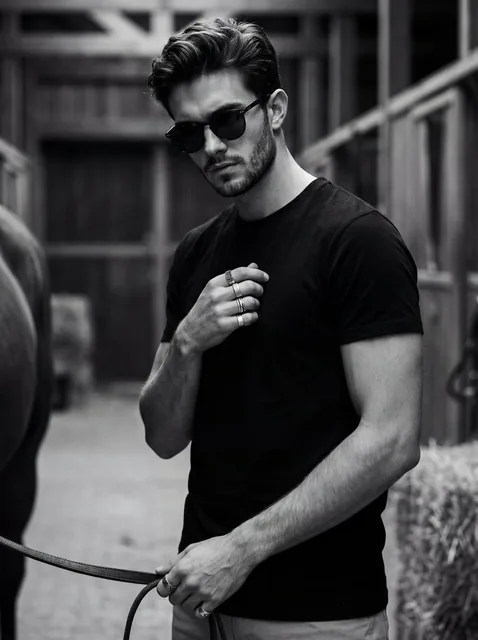 Ultra-realistic 8K cinematic black-and-white portrait of a young man with a lean physique, wearing sunglasses, in an attitude-heavy pose, looking downwards.