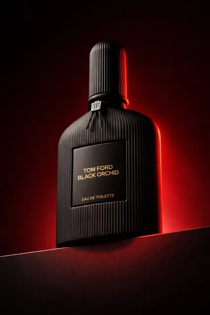 Low angle luxury product photography of a black ribbed glass perfume bottle placed on a dark horizontal podium, shot fro
