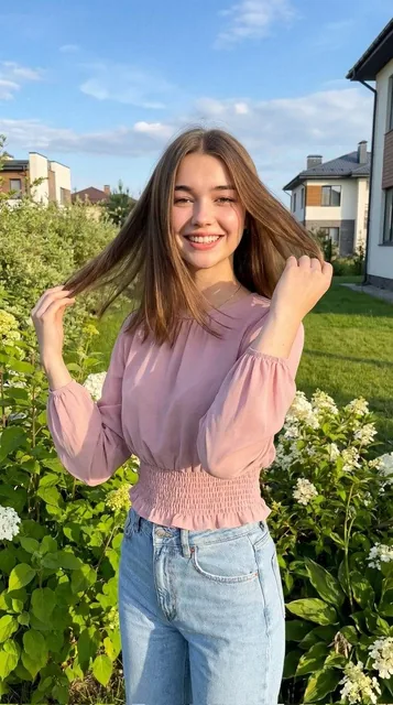 A cheerful young woman standing outdoors in a lush green garden, smiling brightly while gently holding her hair with bot