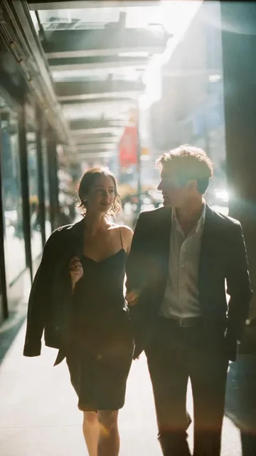A cinematic candid medium shot portrait of a man and a woman walking side by side along a bright urban walkway, framed f
