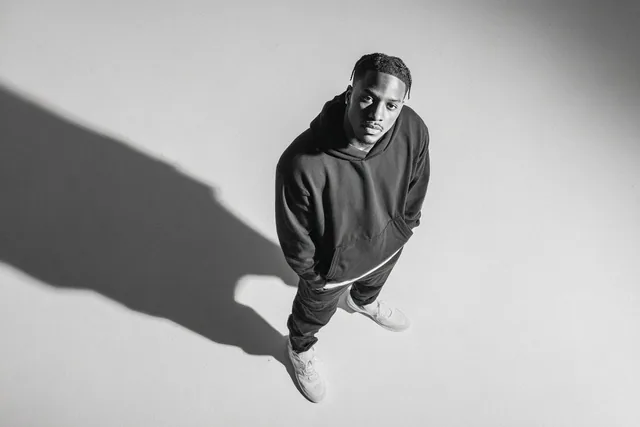 A [subject] photographed from a 35-degree overhead angle, standing alone in an off-white studio void, with a confident p