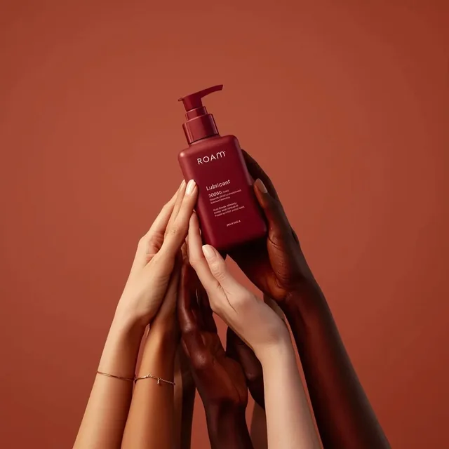 Minimalist product photography of a matte red pump bottle labeled ‘ROAM lubricant’, held by multiple diverse hands with