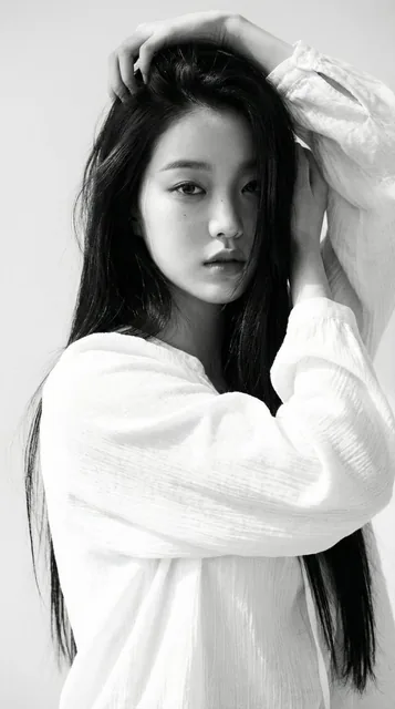 Black-and-white portrait of a young woman with long straight dark hair, wearing a loose white blouse, softly lit with na