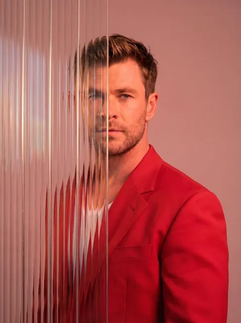 A striking editorial portrait photograph of a person wearing a red blazer, shot against a soft light pink studio backgro