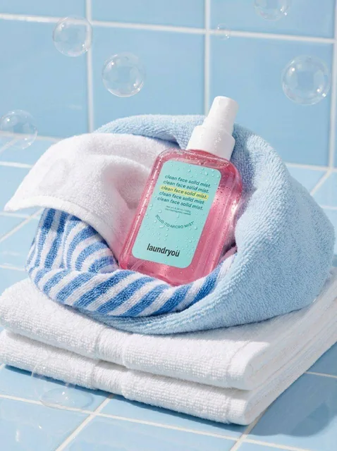 A translucent pink facial mist spray bottle with a white cap, covered in tiny condensation droplets, lying diagonally on