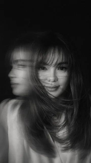 A hyper-realistic, cinematic black-and-white portrait of a woman caught in mid-motion, her face partially obscured by sw