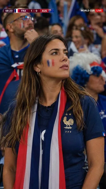 Ultra-realistic live football broadcast cutaway captured inside a packed World Cup stadium. A beautiful French female su