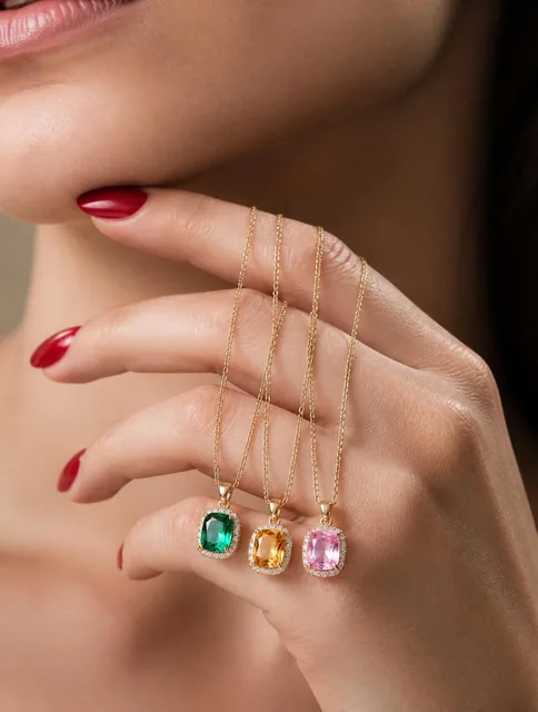 A close-up portrait features a woman’s hand gracefully cradling three delicate pendant necklaces, their faceted emerald,