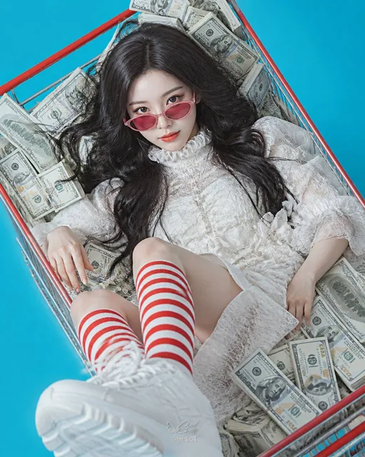 High-angle portrait of a young woman lying inside a red and silver metal shopping cart overflowing with stacks of dollar