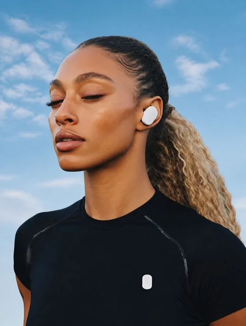 Confident woman with wireless earbuds in a blueish sky background, wearing a black athletic shirt, with semi-closed eyes