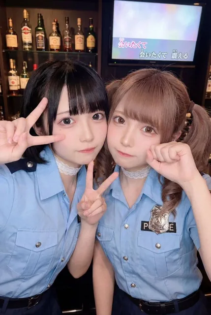 A realistic and cute selfie of two young Japanese women in light blue police cosplay, posing cheek-to-cheek in a dimly lit bar with a karaoke monitor in the background, featuring soft lighting and a 2016 Jirai-kei aesthetic.