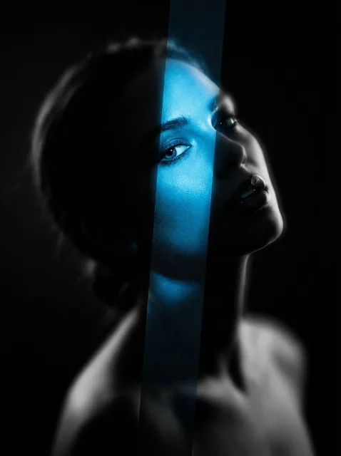 An avant-garde noir portrait of a woman with her head thrown back. A sharp vertical strip of vibrant electric blue light cuts through her face, revealing hyper-realistic detail with film grain, while the rest of her form dissolves into deep black, heavily blurred shadows against a void background.
