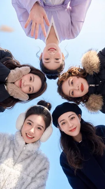 A group of five friends forming a circle, viewed from an extreme low angle against a pure blue sky. The two girls closest to the camera at the bottom have distinct, cheerful expressions and wear winter accessories like white earmuffs and a black beret.