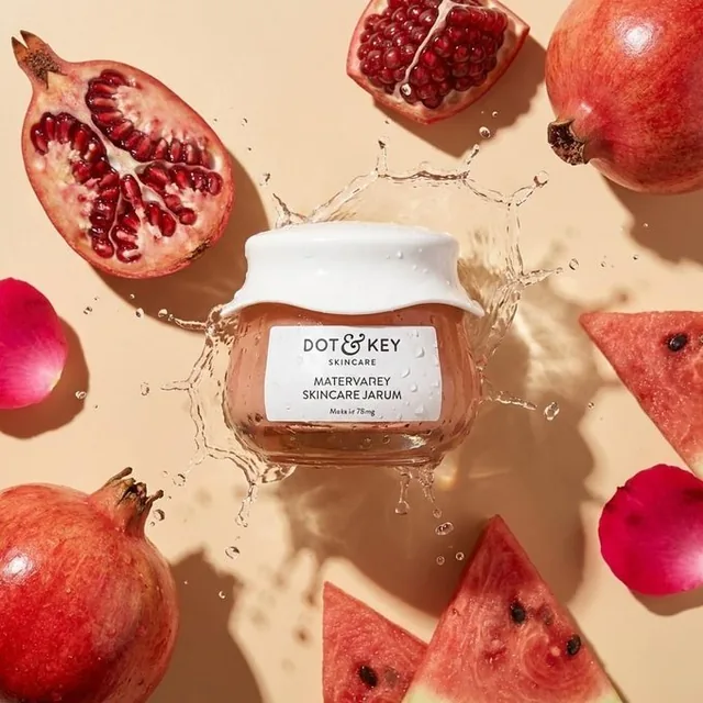 An ultra-realistic high-end skincare product flat lay advertisement. The product is centered with fresh ingredient slices and whole pieces around it, featuring a glossy wet look, frozen water splashes in motion, and dewy droplets on the label and surfaces, all set against a warm beige background wit