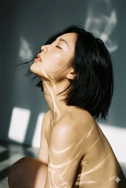 Close-up cinematic film portrait of a young Asian woman in profile, head tilted back, eyes closed, with wispy black hair and bare shoulders illuminated by sharp caustic light strea