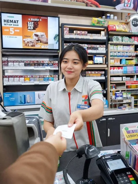 A photorealistic candid smartphone POV shot of a young Japanese female cashier in a convenience store uniform, serving a customer with a natural expression, with POS terminal and snacks on the counter.