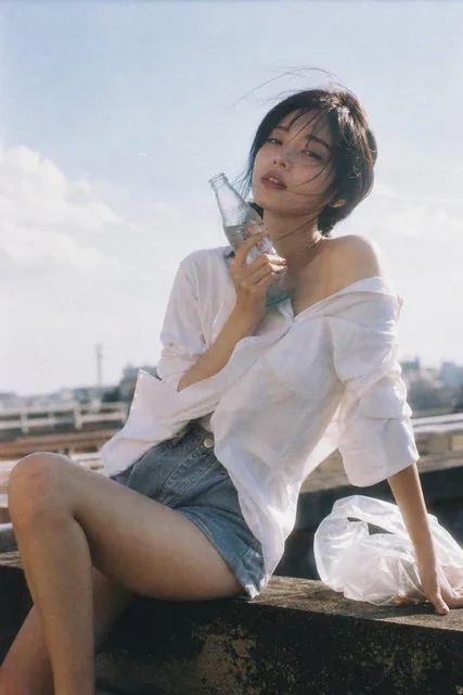 A stunning young woman on a summer rooftop, wearing an oversized white shirt and high-waisted shorts, holding a cold glass bottle, with soft natural sunlight and film grain aesthetic, nostalgic and reflective mood