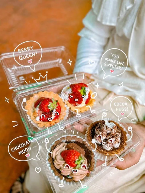 Close-up of colorful pastries and desserts in a cozy café, with adorable white doodle-style cartoon overlays including kawaii faces, hearts, and speech bubbles, warm ambient lighting, soft bokeh background.