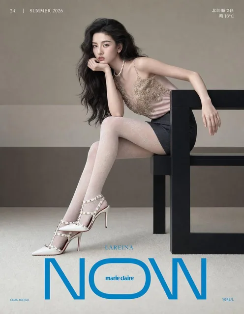 A young East Asian female fashion model in a pale blush satin camisole and dark charcoal mini skirt, seated sideways on a black bench, with a direct confident gaze, on a minimalist magazine cover with cyan blue masthead and typography.