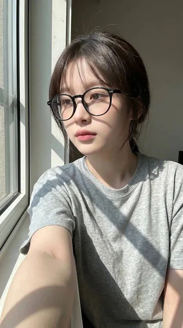 Ultra-realistic candid smartphone selfie portrait of a young East Asian woman sitting indoors beside a large window during bright natural daylight, with strong facial resemblance to uploaded reference.