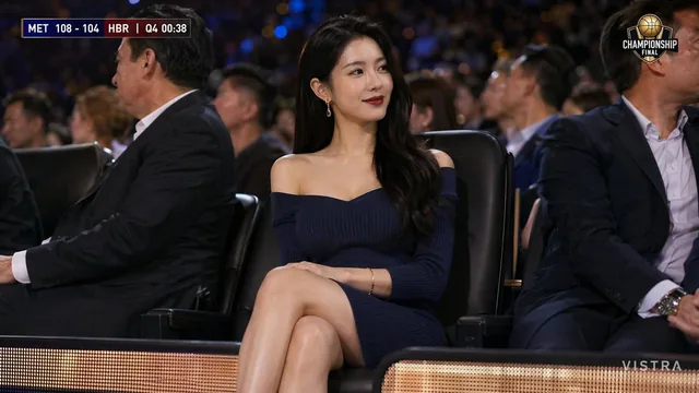 A photorealistic broadcast-style screenshot from a live national TV sports broadcast of a major international football championship final. A stunning East Asian woman with long wavy black hair, fair skin, and elegant makeup throws her head back in an explosive joyful cheer in the front row of a pack