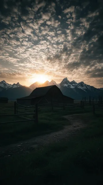 Dark wooden barn silhouetted against a glowing sunrise, dramatic sky with textured scattered cl...