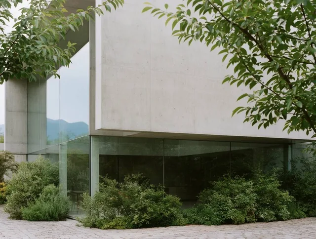 A minimalist modern building features smooth concrete walls and expansive glass panels nestled...