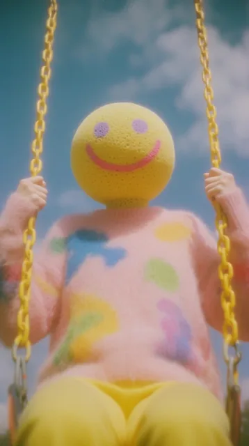 humanoid figure with a spherical yellow sponge-textured head featuring purple dot eyes and a pi...