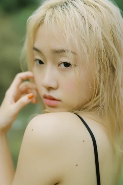A close-up film photography portrait of a young East Asian woman looking over her bare left sho...