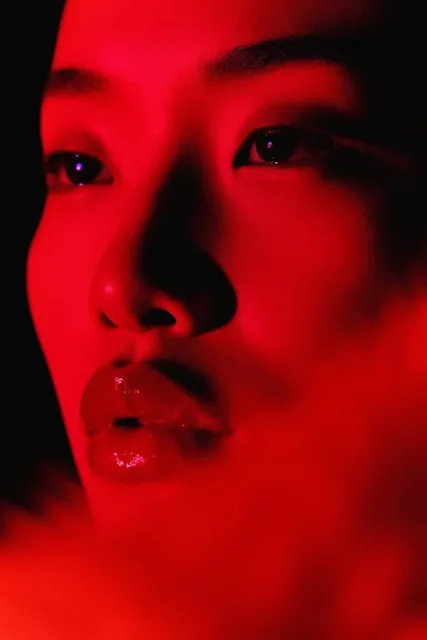 Extreme close-up face bathed in intense red light against a pitch-black background. The subject...