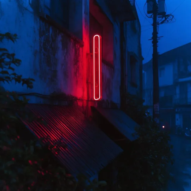 Vertical red neon tubing on a weathered building facade, deep cobalt blue night atmosphere, cri...
