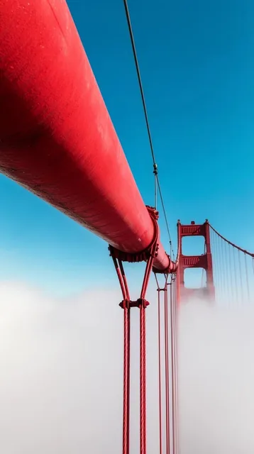 massive red suspension bridge cable spanning diagonally across a vivid blue sky, vertical wire...