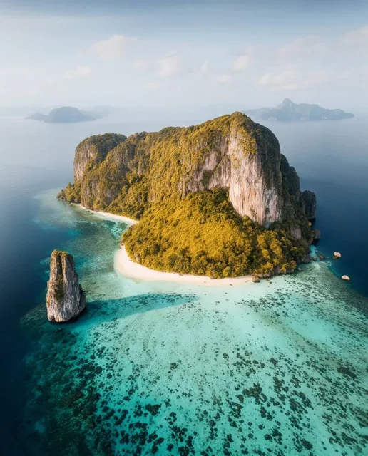 aerial view of a lush tropical island, massive central limestone cliff covered in golden-green...
