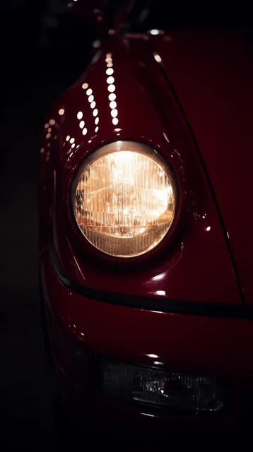 A dramatic, tight close-up of a classic sports car's front quarter panel finished in deep, glos...